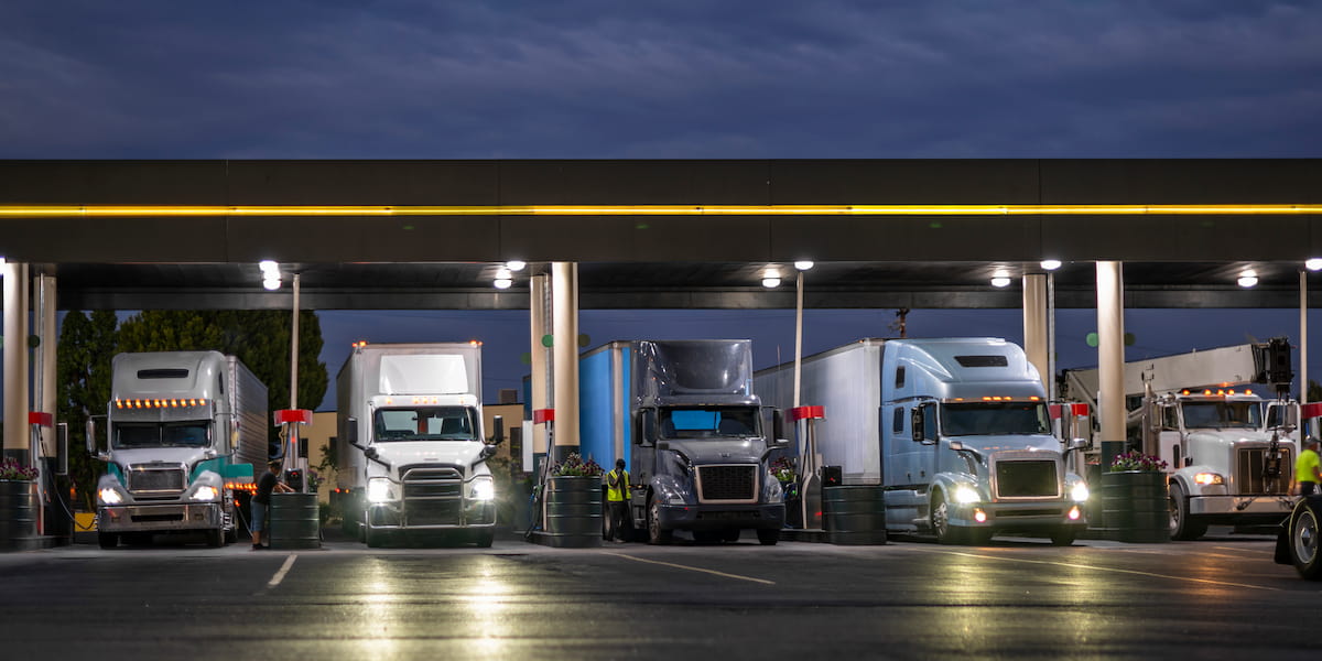 Row of semi-trucks refueling at a gas station at night, highlighting the long-haul conditions and fatigue risks that can contribute to truck crashes.